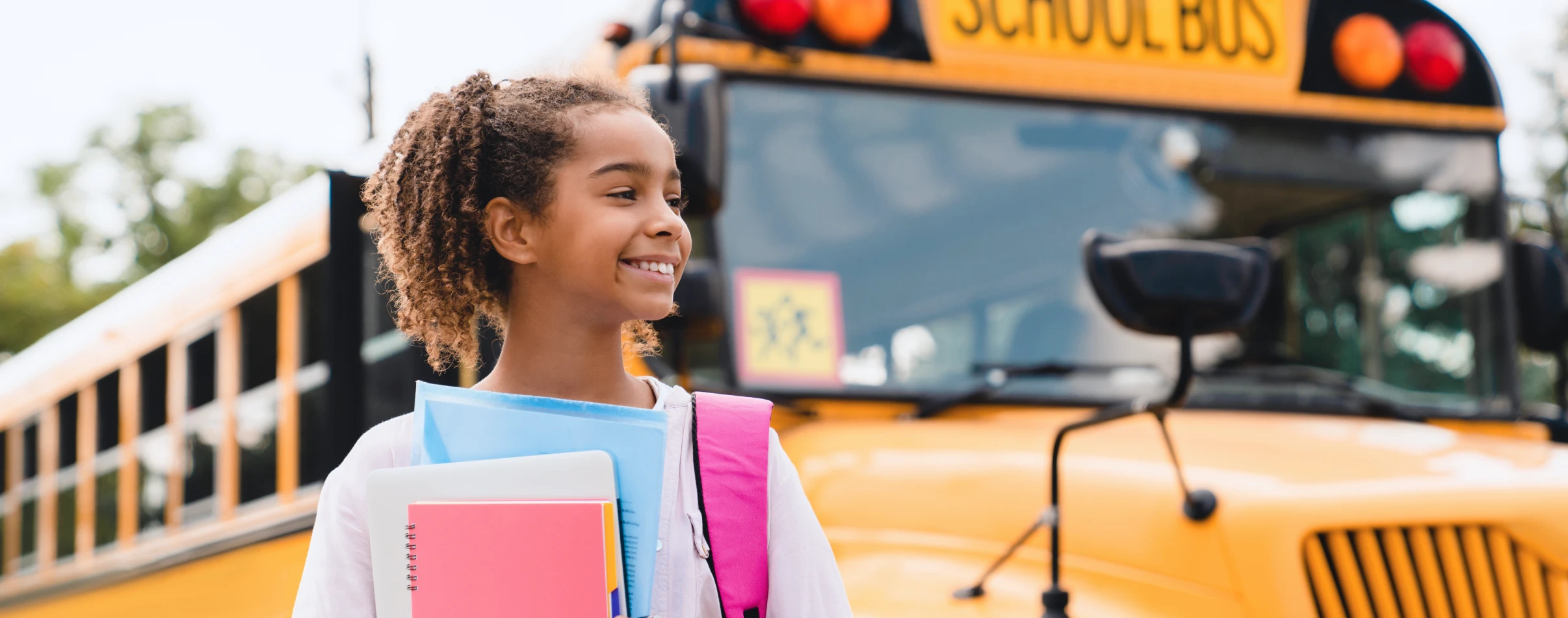 A smiling student stands near yellow school bus