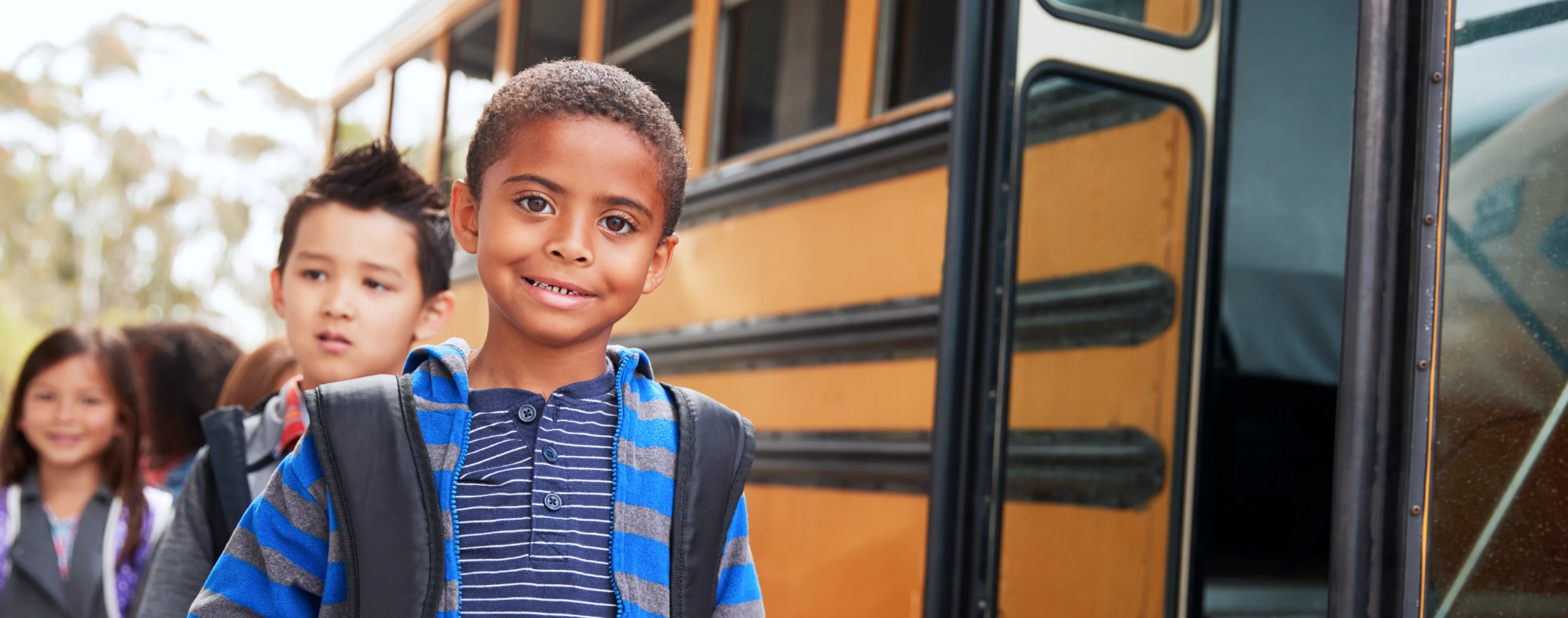 Students smile next to yellow school bus.