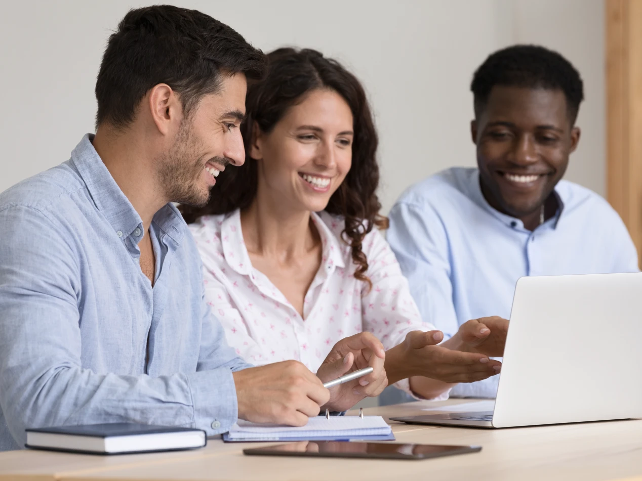 Three administrators sit together at a desk, smiling while viewing a laptop.