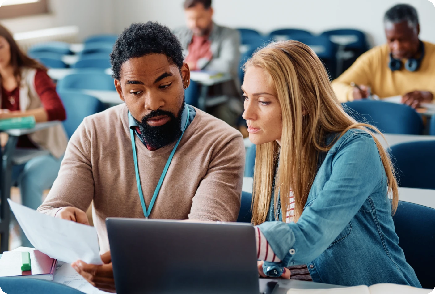 2 people sitting at a desk looking at a computer and some paperwork