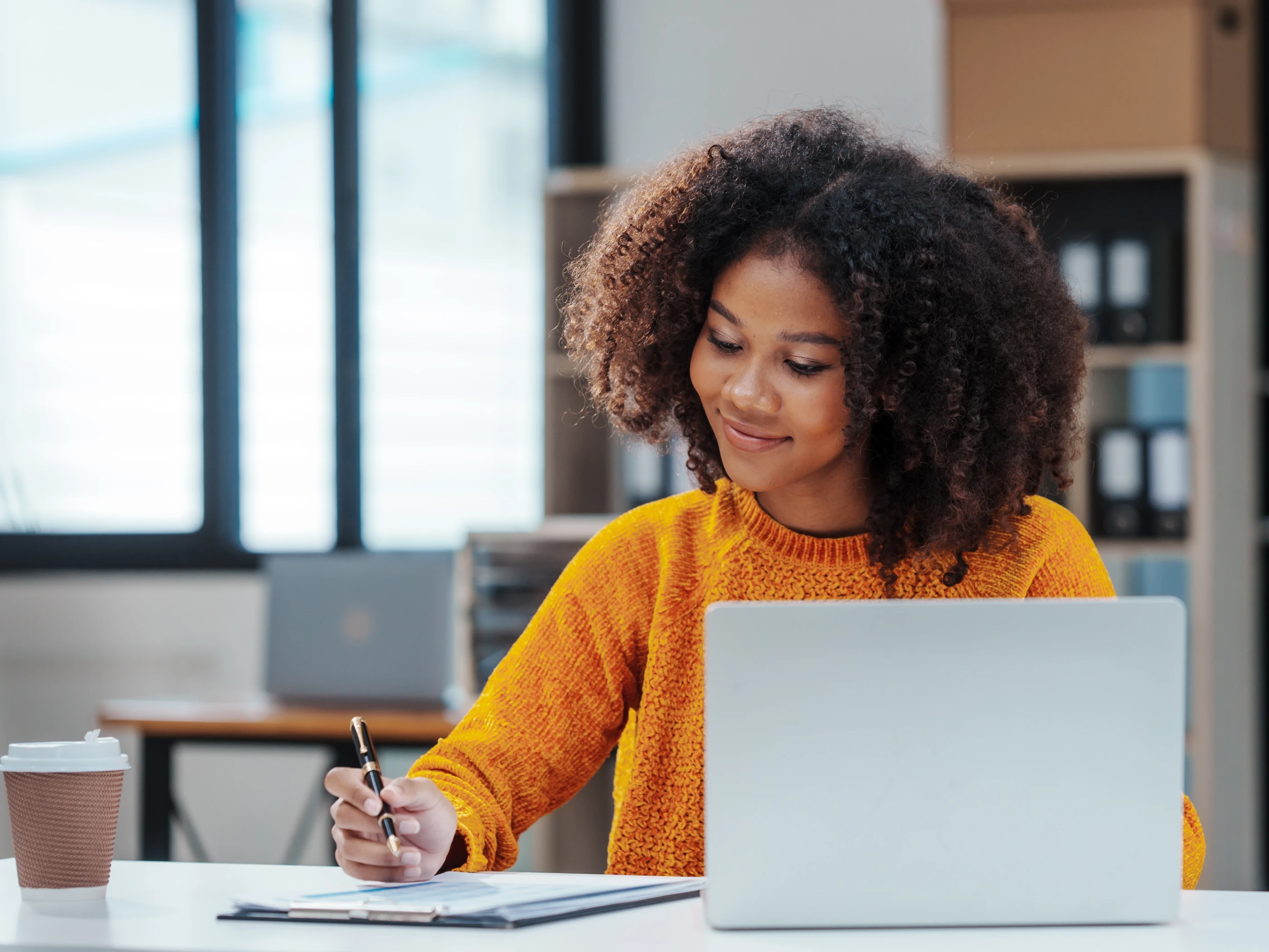 Smiling woman works at a desk with laptop.