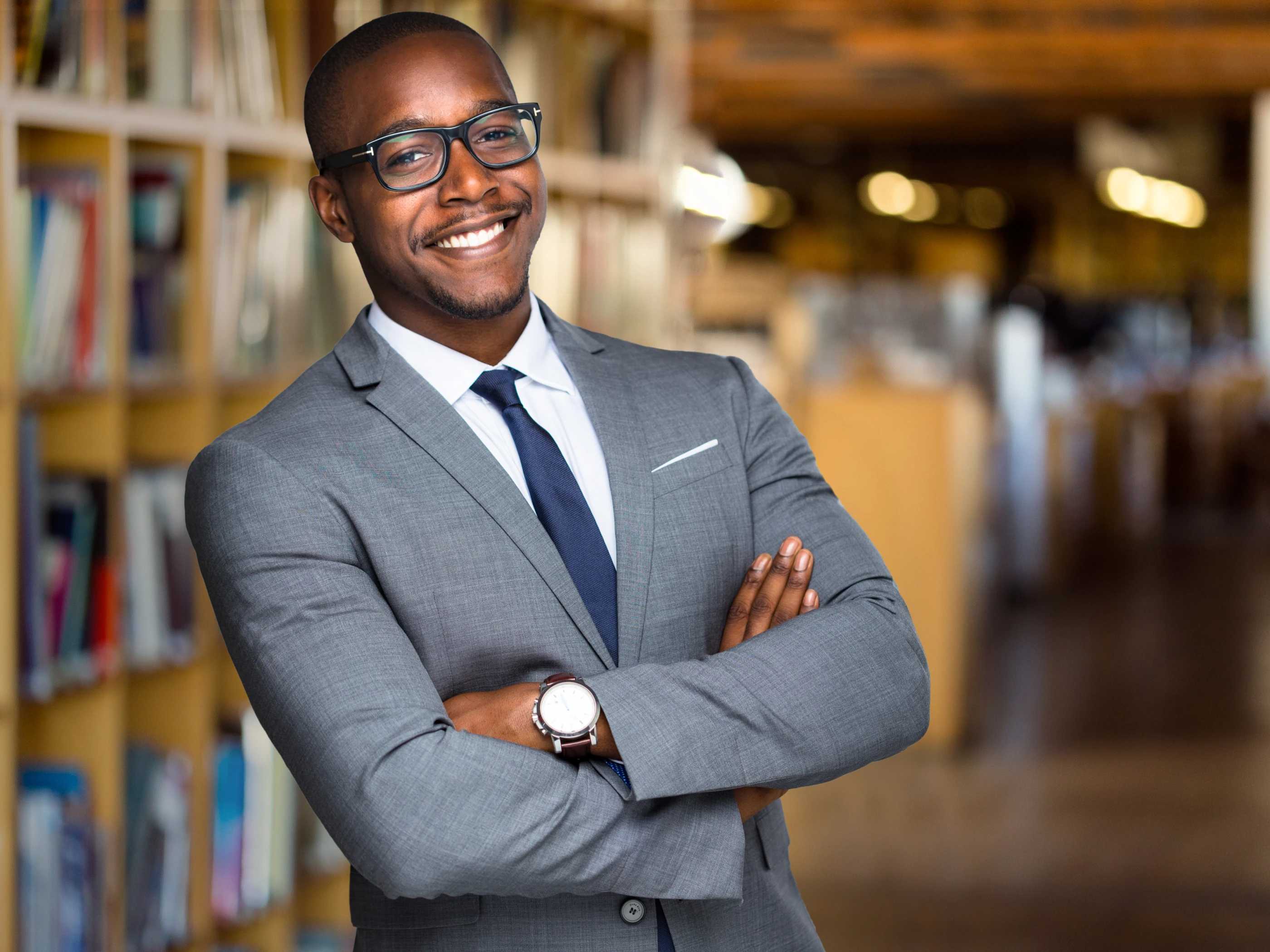 A smiling administrator in a suit stands with arms crossed.