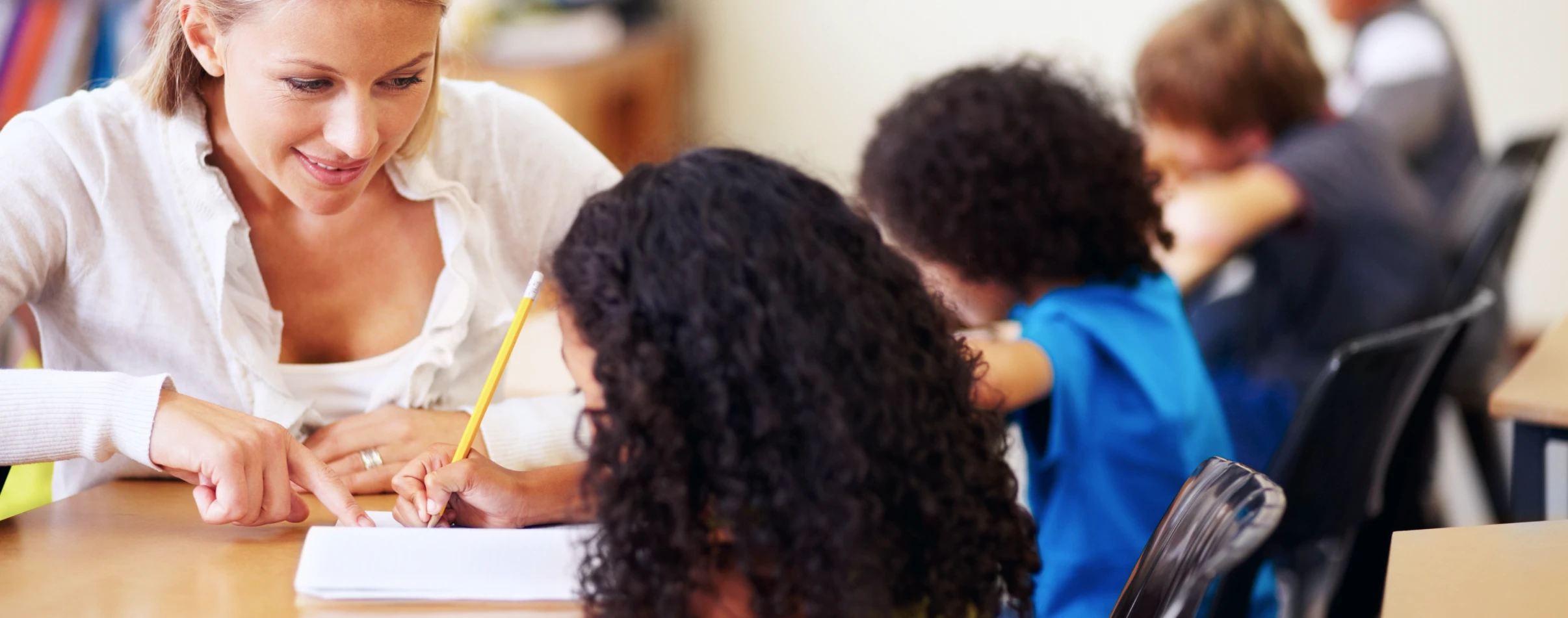 School teacher sits at a desk with students.